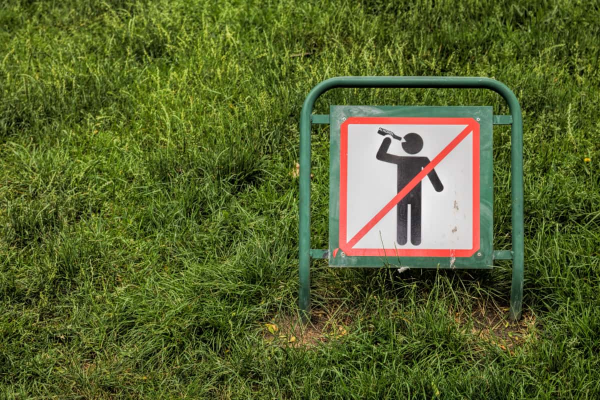 stick figure holding bottle to mouth on a sign with a red box and line through it.